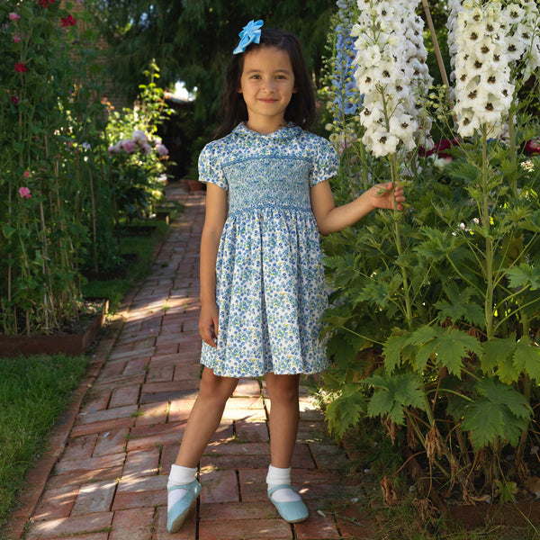 Girl in blue floral dress with hand-smocked bodice, peter pan collar and gathered skirt.