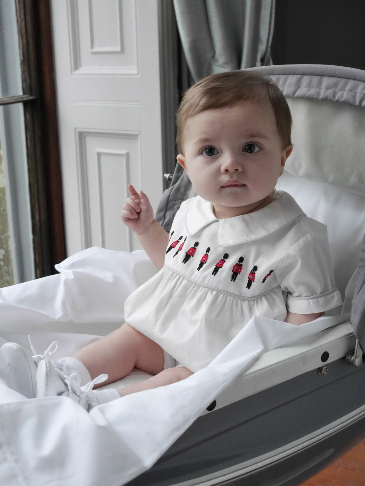 Baby boy in ivory babysuit with soldier embroidered motif on chest and grey piping at collar and cuffs