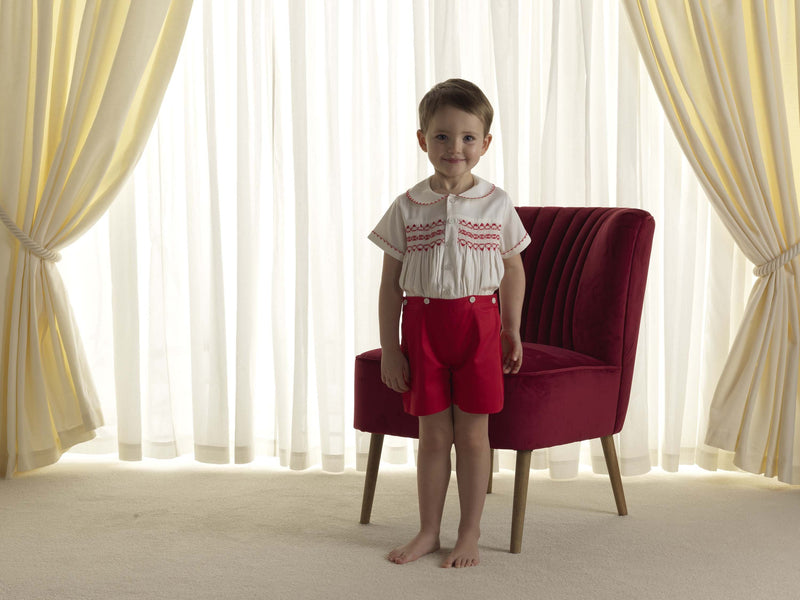 Boy wearing red smocked, short sleeved shirt and matching red button on short set