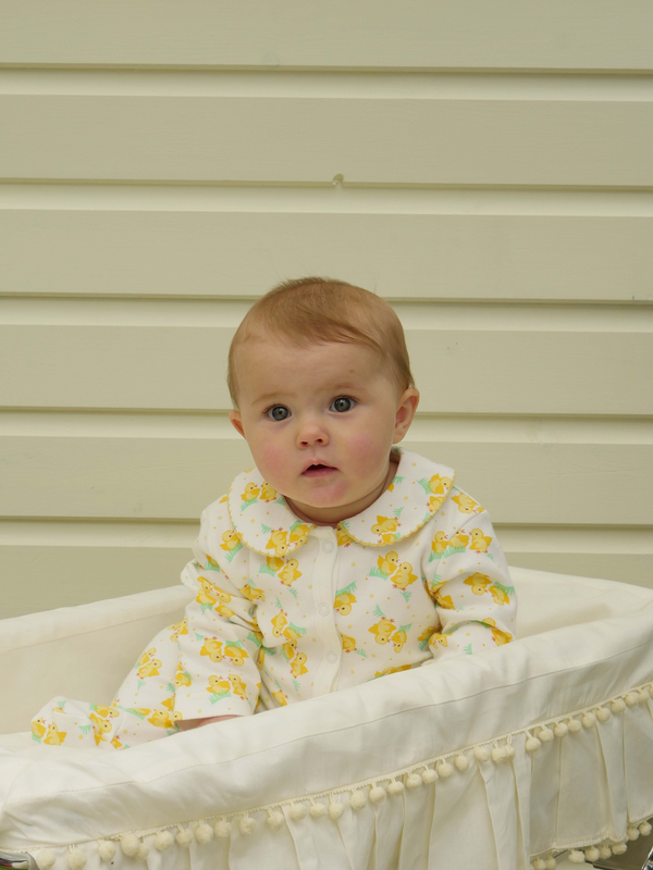 Baby wearing soft cotton babygro with yellow chicks print on white base.