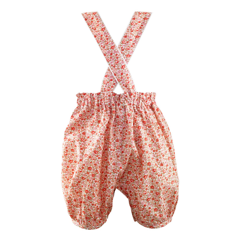 Coral pink frill dungarees with floral print and ivory piping trim, and adjustable crossover straps.