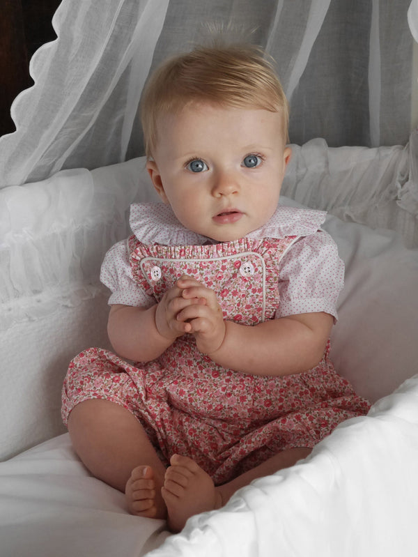 Baby wearing coral pink frill dungarees with floral print, styled with ivory picot trim body.