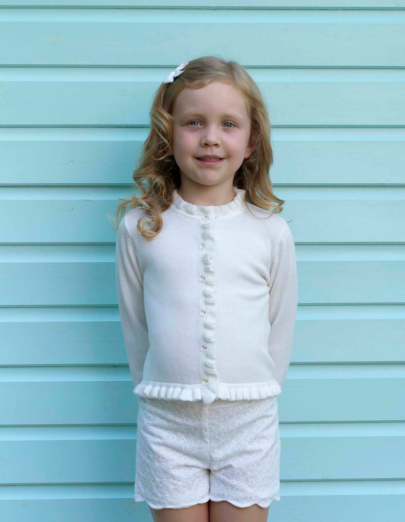 Girl in ivory frill cardigan and matching scalloped shorts and hairbow.