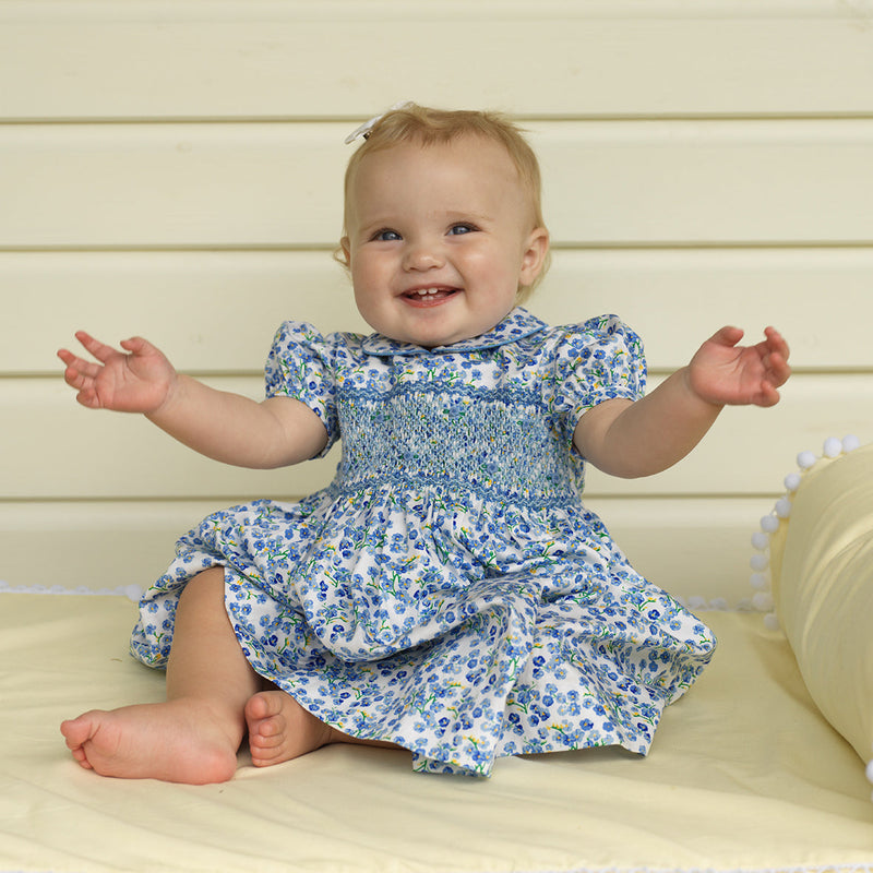 Baby in blue floral dress with hand-smocked bodice, peter pan collar and gathered skirt.