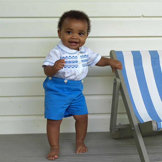 Baby boy wearing blue smocked, short sleeved shirt and matching blue button on short set