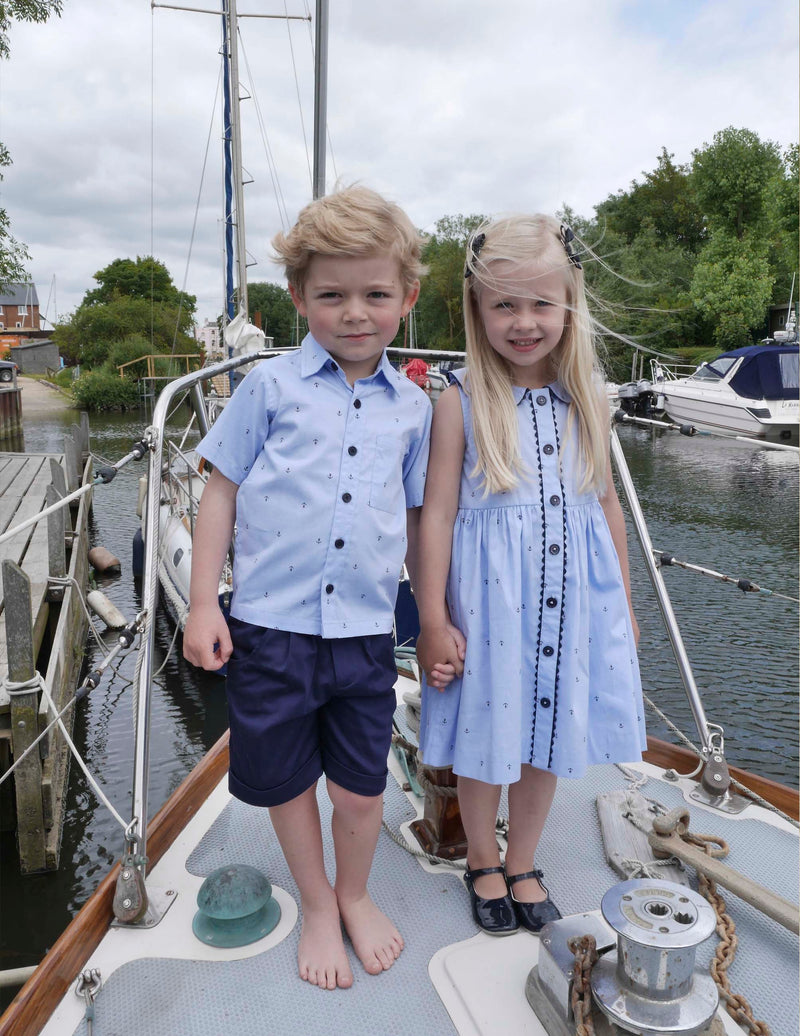 Boy in blue short-sleeved oxford shirt with mini anchor print and navy tailored shorts.