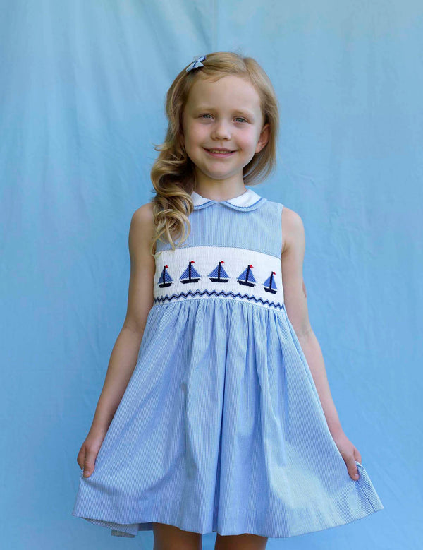 Girl in sleeveless dress with blue and ivory stripes, hand-smocked sailboat design and peter pan collar.