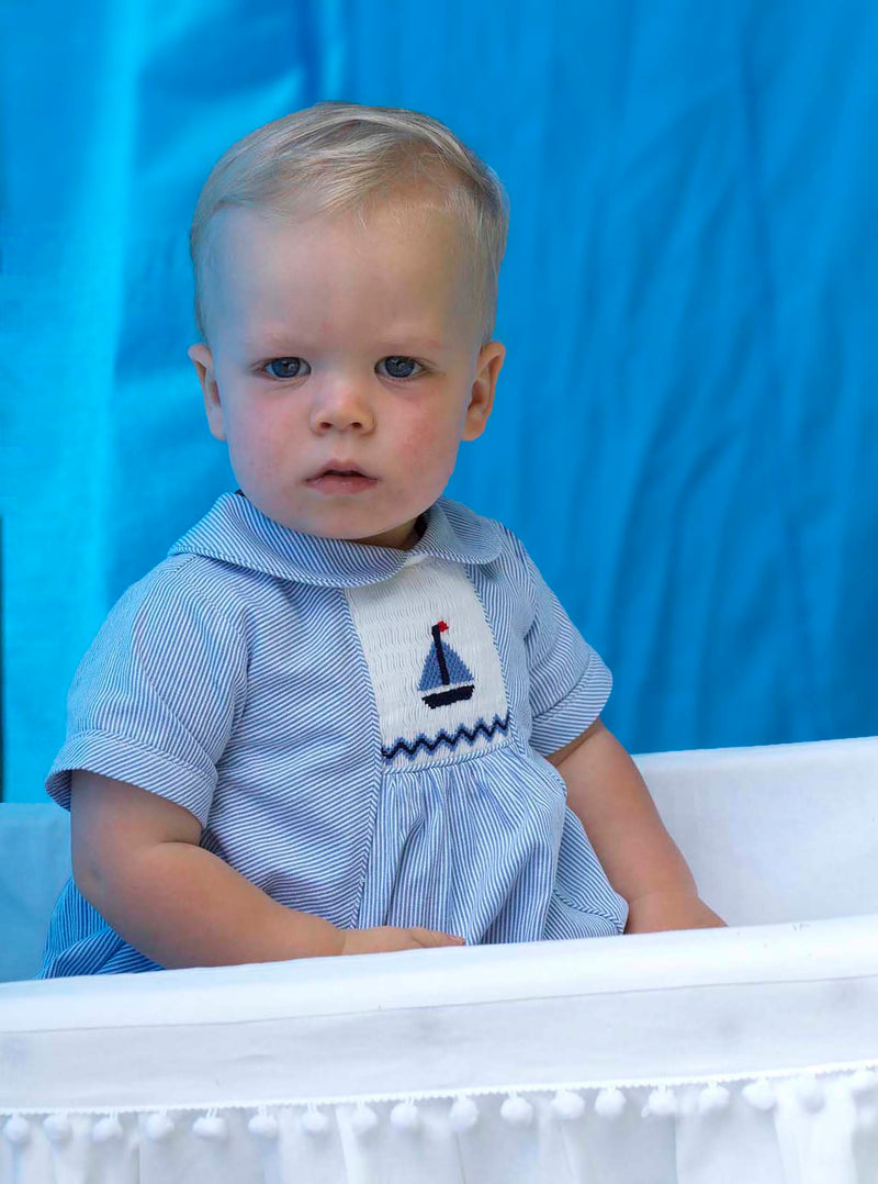 Baby boy in blue striped babysuit with sailboat smocked motif on the chest and peter pan collar