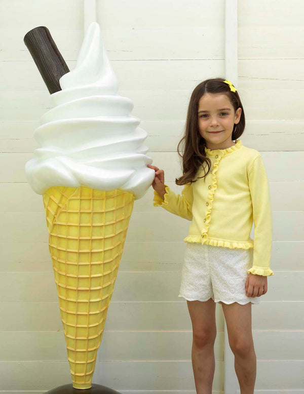 Girl wearing yellow frill cardigan styled with ivory scalloped shorts and matching hairbow.