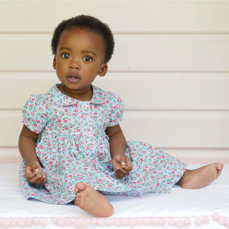 Baby in floral button front dress in blue and pink, with puff sleeves and ricrac trims and buttons.