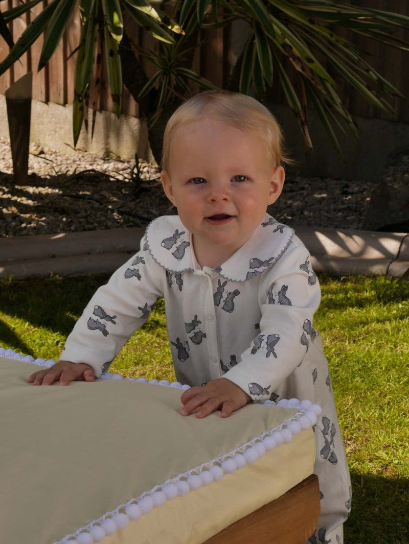 Baby wearing soft cotton babygro with grey bunnies print on white base.