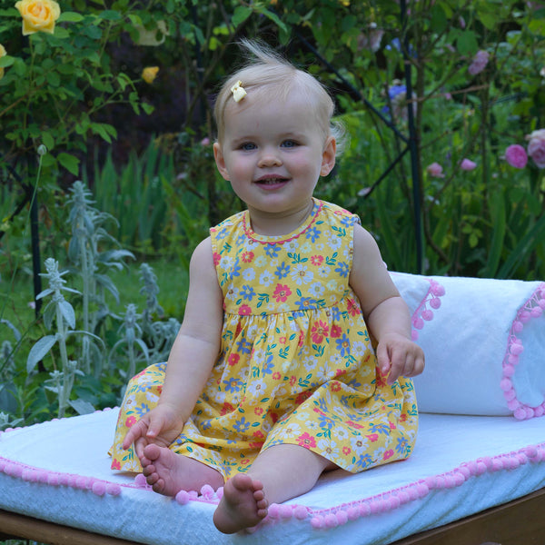 Baby in cotton sleeveless dress in floral design on yellow background and gathered skirt.