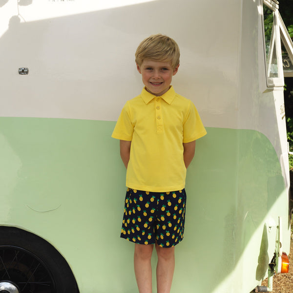 Boy wearing navy shorts with pineapple print styled with yellow polo shirt.