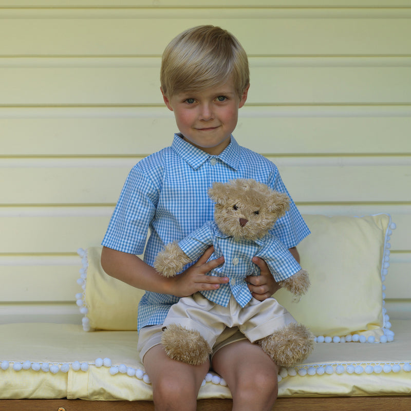 Boy wearing blue gingham shirt styled with beige tailored shorts, and teddy bear in matching outfit.