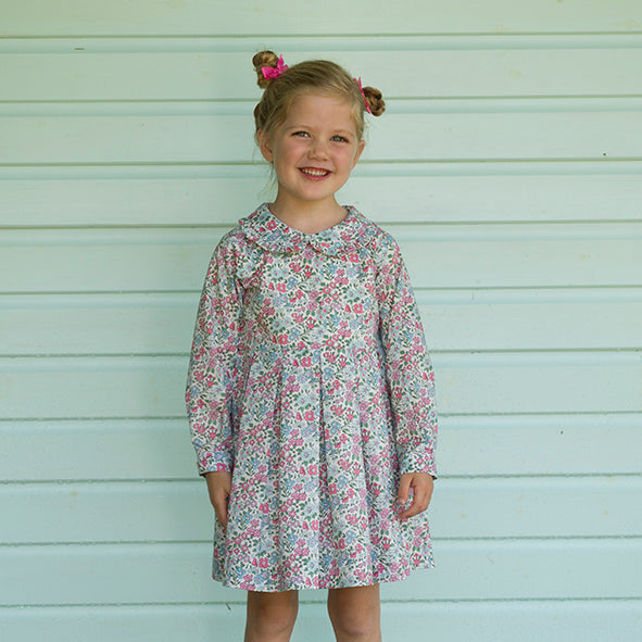 Girl in pink and blue floral pleated dress, long sleeves, peter pan collar and sash tie at the back