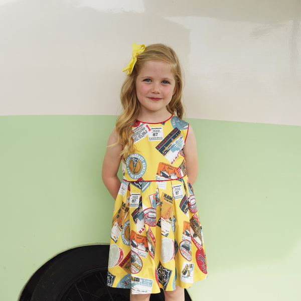 Girl wearing yellow travel stamp dress styled with red slippers and hairbow