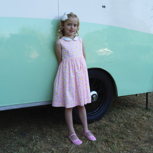 Girl in pink sleeveless dress with daisy print and contrasting ivory peter pan collar.