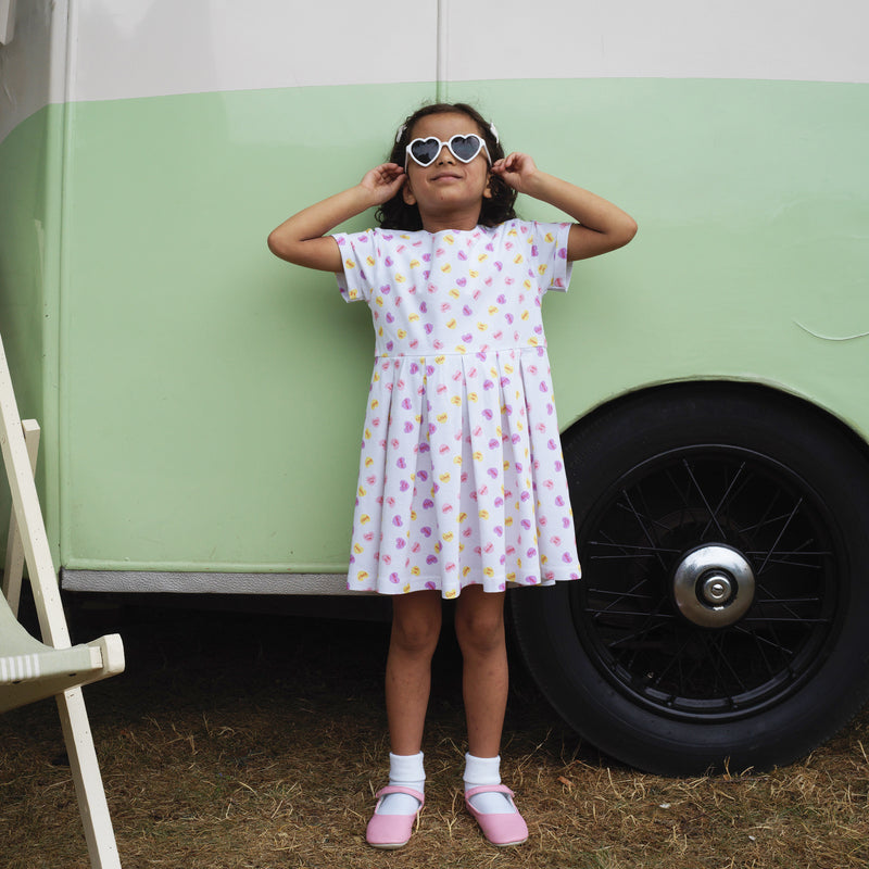 Girl in soft cotton jersey dress with playful heart print on ivory base and pleated skirt.