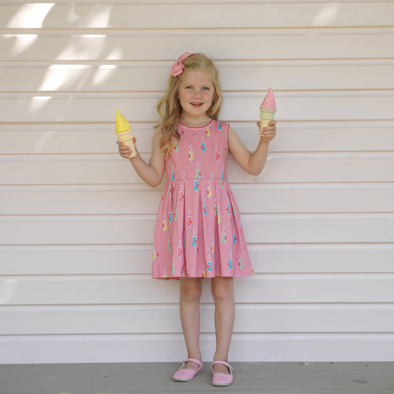 Girl in pleated jersey dress with colourful soda pop print on pink base.