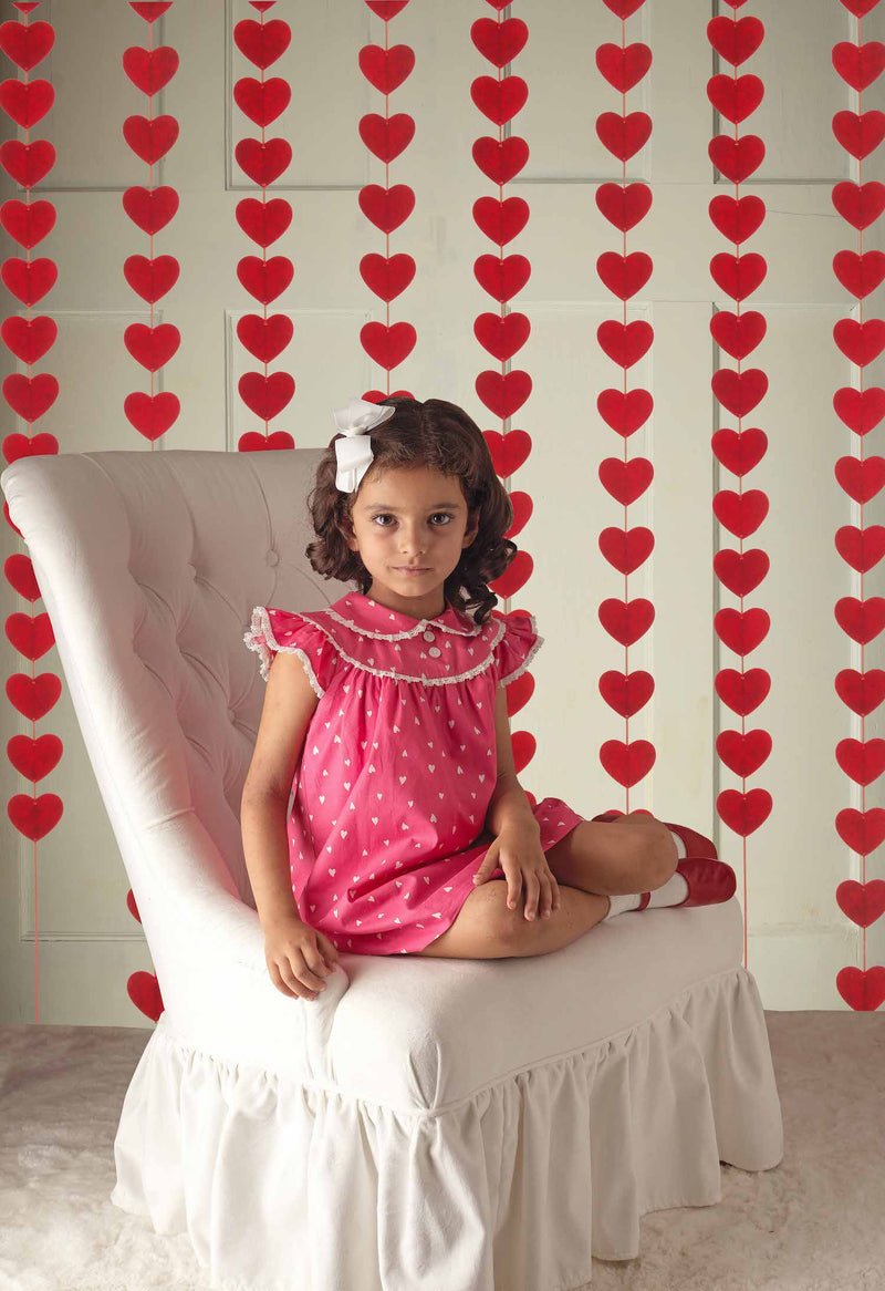 Girl wearing pink lace trim heart dress styled with matching pink slippers and white haibow.