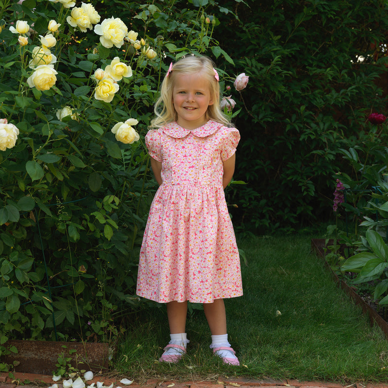 Girl in pink floral print dress with frill on the bodice and collar, and puff sleeves.