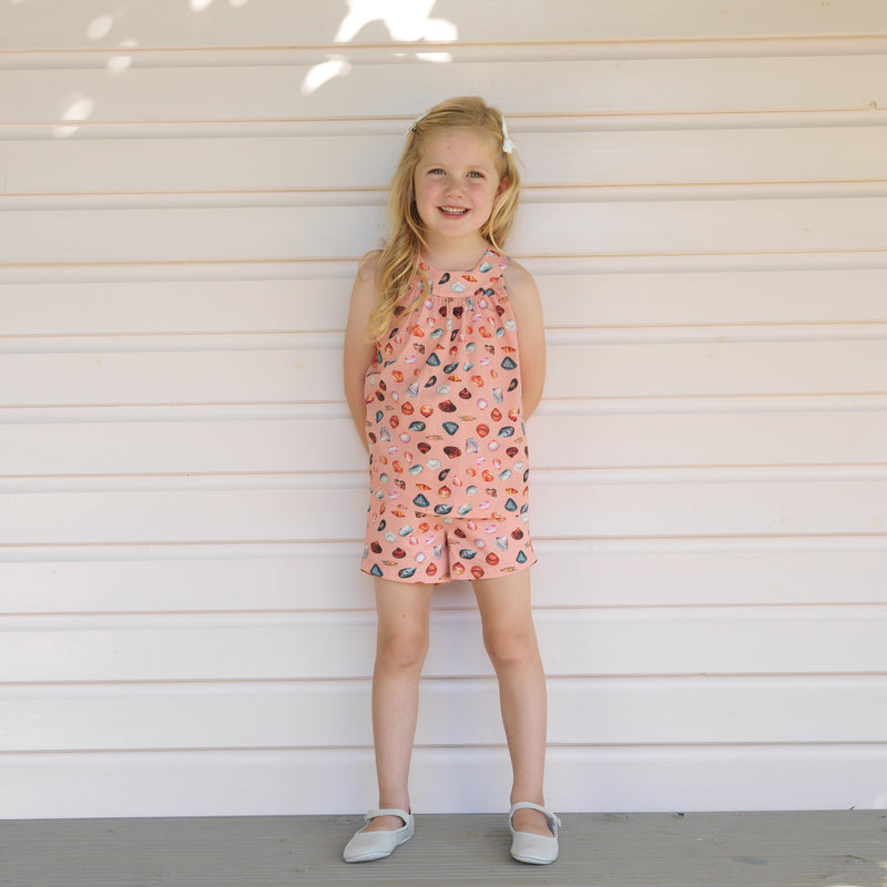 Girl in top & shorts set featuring a vibrant sandy beach print on coral pink base.