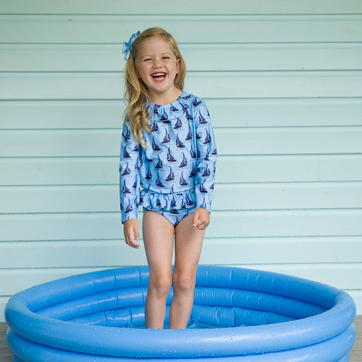Girl two piece rash guard with long sleeves and frill bottom, with sailboat print on blue background
