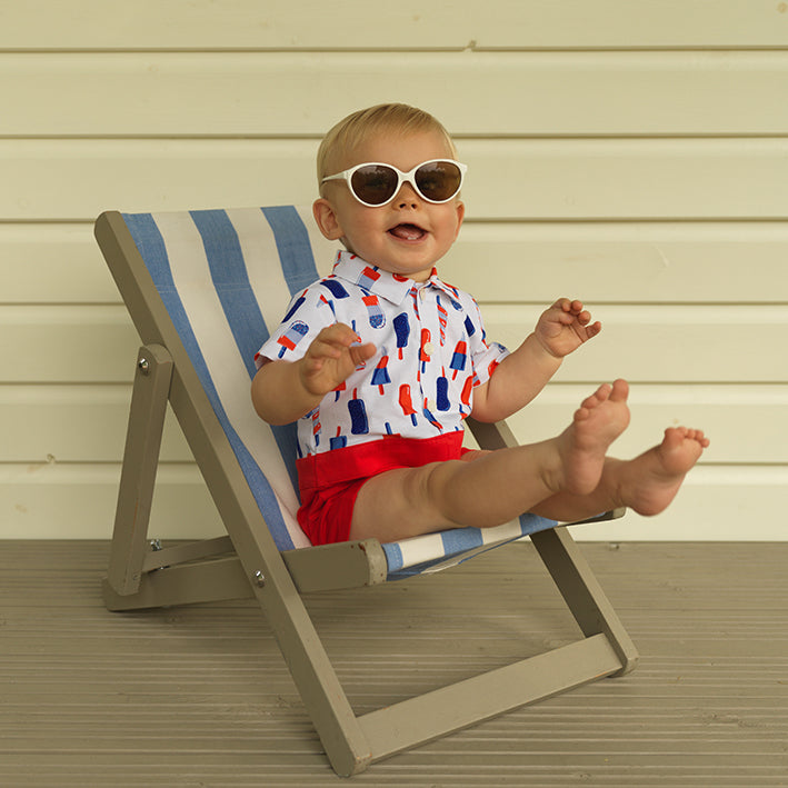 Baby boy wearing short-sleeved ice lolly print romper and matching sunglasses.