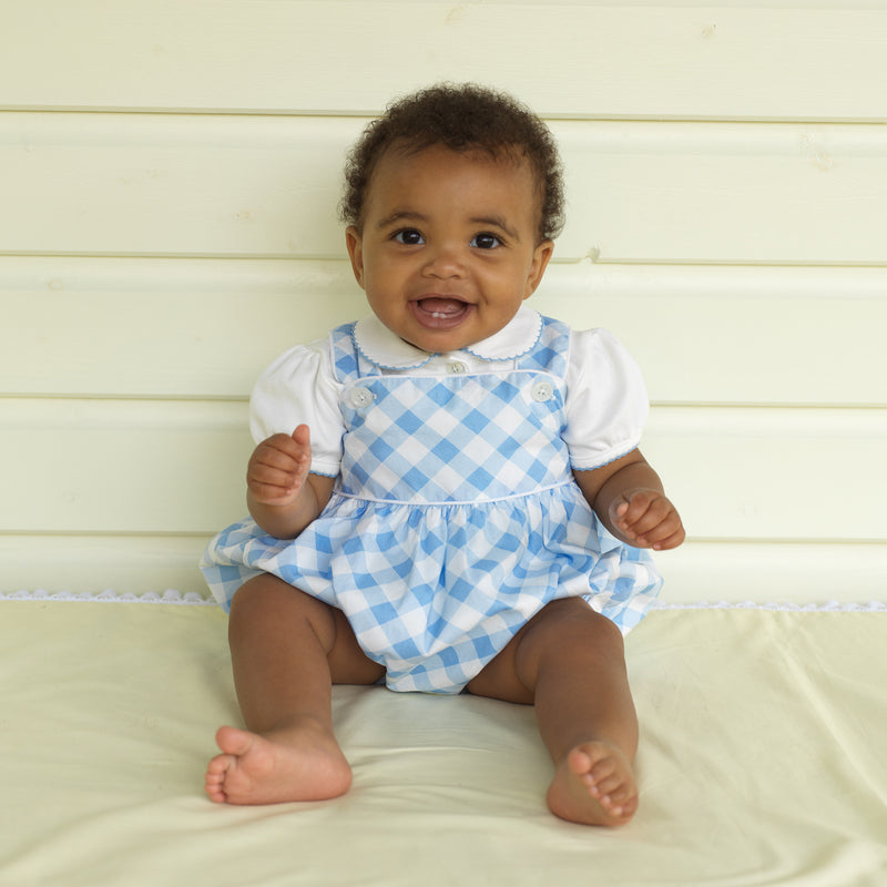Baby wearing blue picot trim shirt, short sleeved, styled with blue checked dungarees.