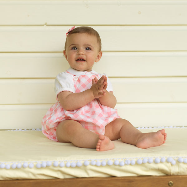 Baby girl wearing pink picot trim bodysuit styled with floral frill dungarees and pink hairbow.
