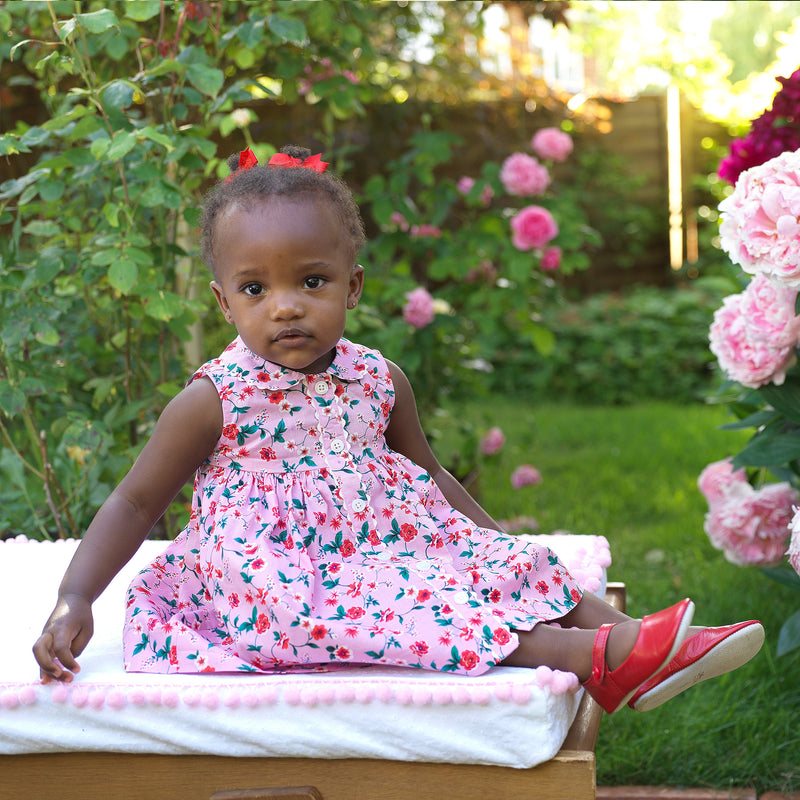Baby wearing pink botanical print button-front dress and matching button strap slippers and hairbow.