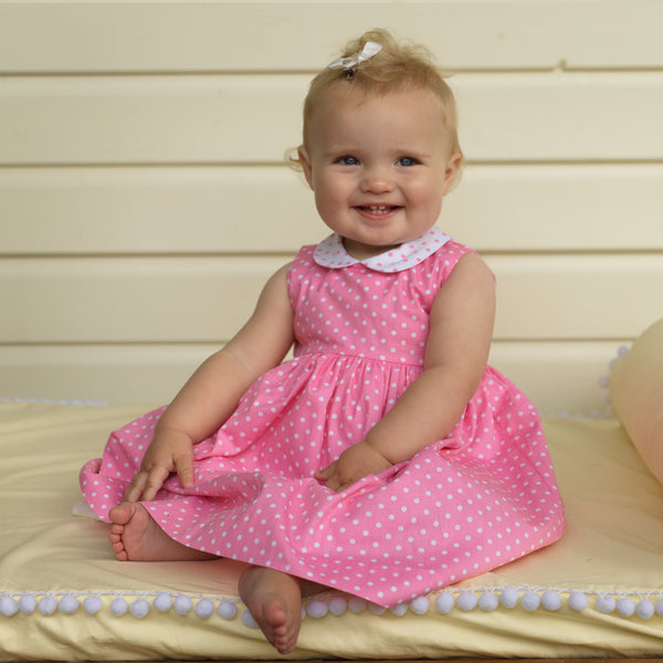 Baby girl wearing pink dotty dress and matching white hairbow.