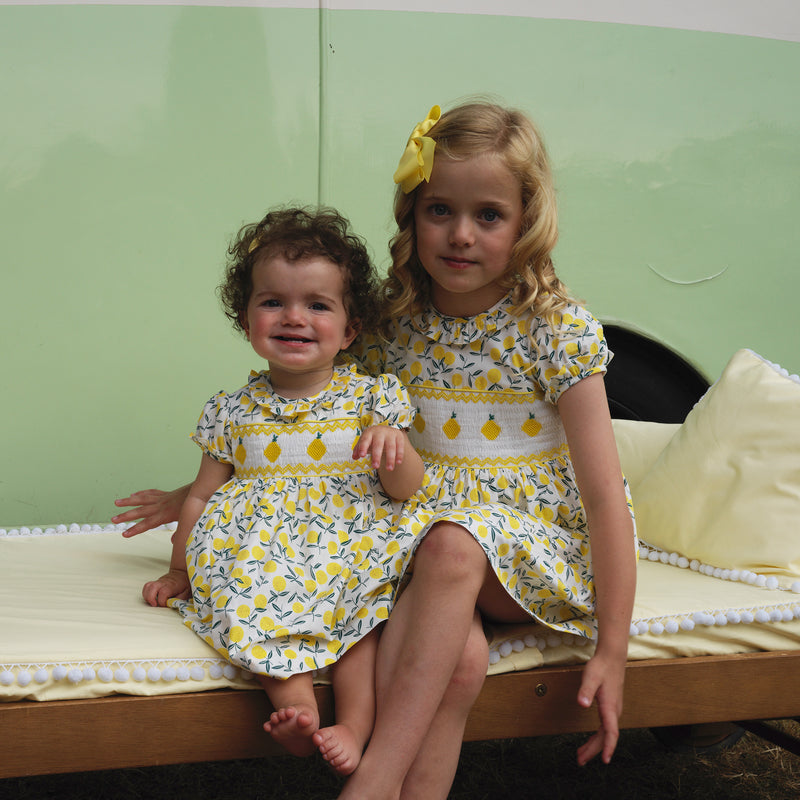 Girl and baby girl wearing matching lemon smocked dresses and complimenting yellow hairbows.