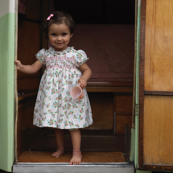 Baby wearing posy floral print dress with smocked bodice, frill collar and puff sleeves.