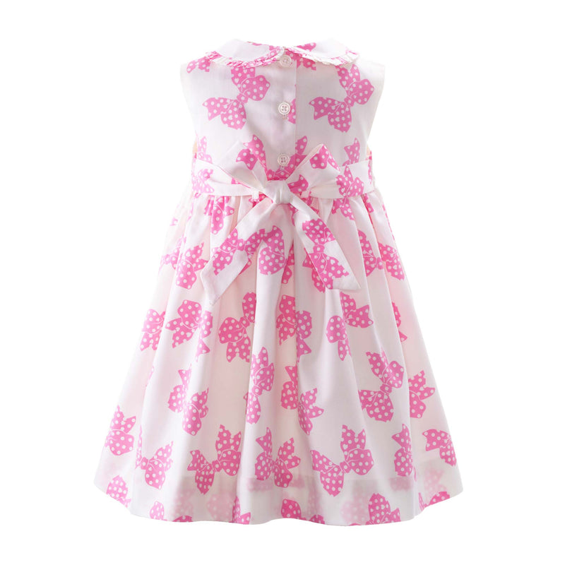 Baby girls sleeveless ivory dress with pink polka dot bow print, with frills at front and collar.