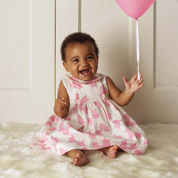 Baby girl wearing pink bow frill dress with matching bloomers.