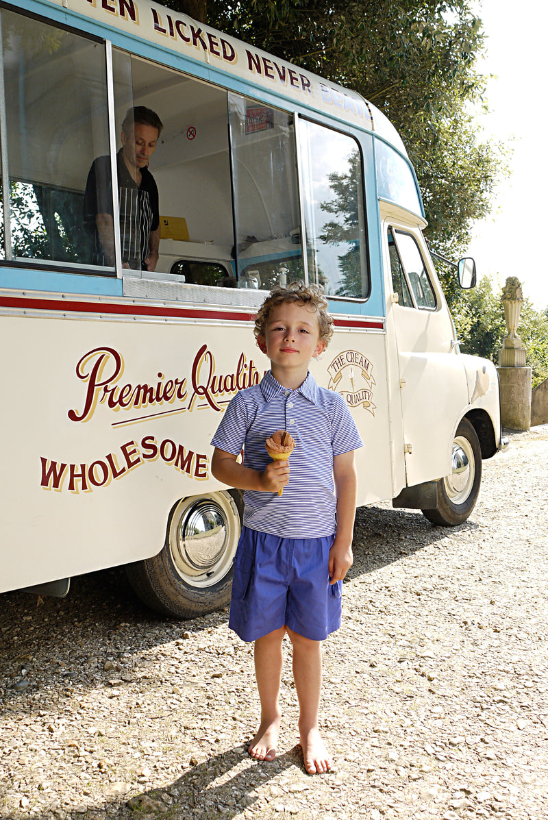 Boy wearing blue cotton poplin shorts with side pockets, and blue striped polo.