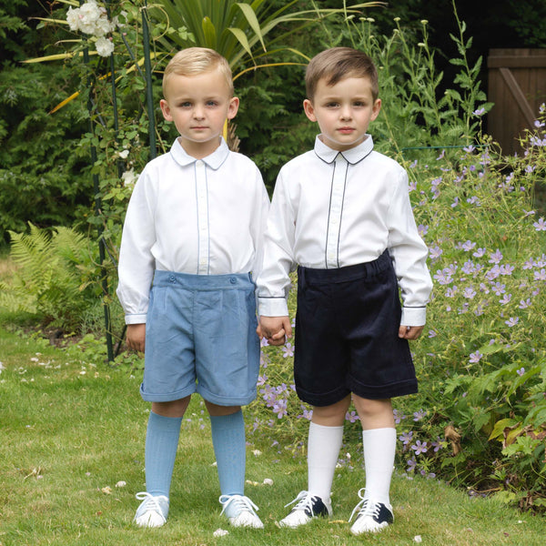 Boy wearing Navy piped pique shirt styled with navy corduroy shorts and white knee socks.