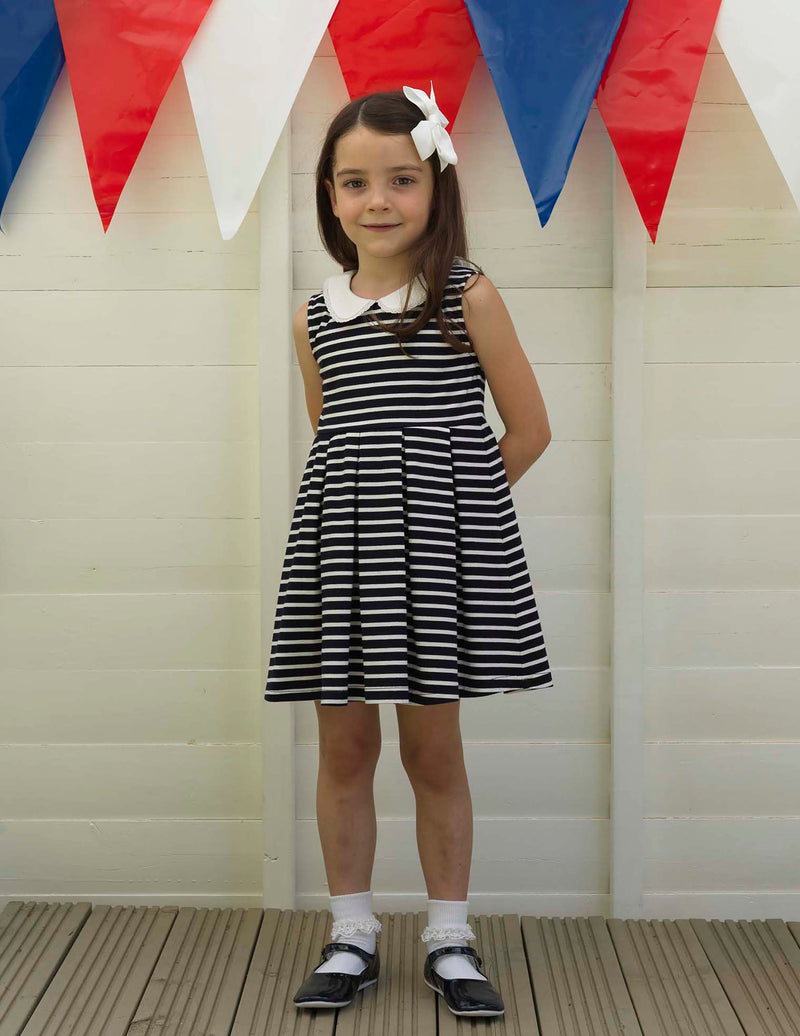 Girl wearing navy sleeveless breton stripe jersey dress styled with navy slippers and white hairbow.