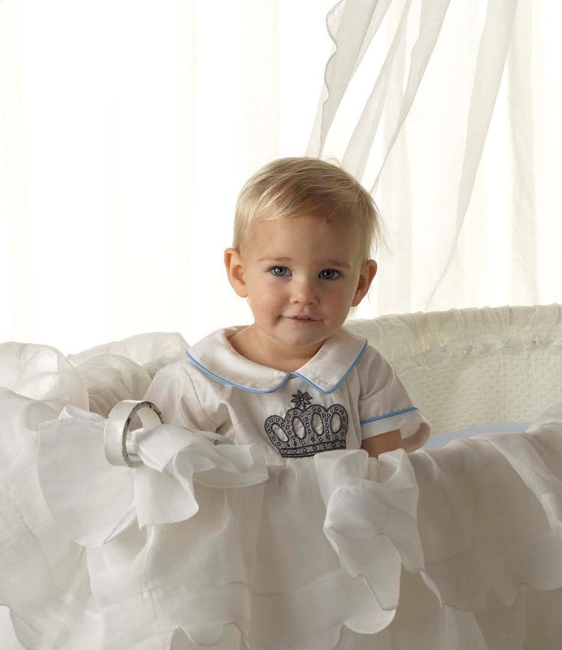 Baby boy in ivory babysuit with crown embroidered motif on chest and blue piping at collar and cuffs