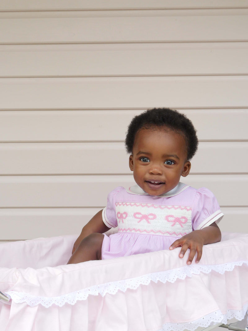 Baby girl in pink and ivory striped babysuit with embroidered bow across the chest. 