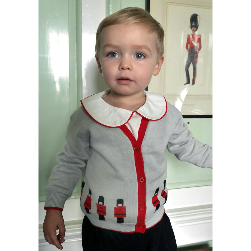 Baby boy wearing soldier intarsia grey cardigan styled with red piping peter pan collar shirt.
