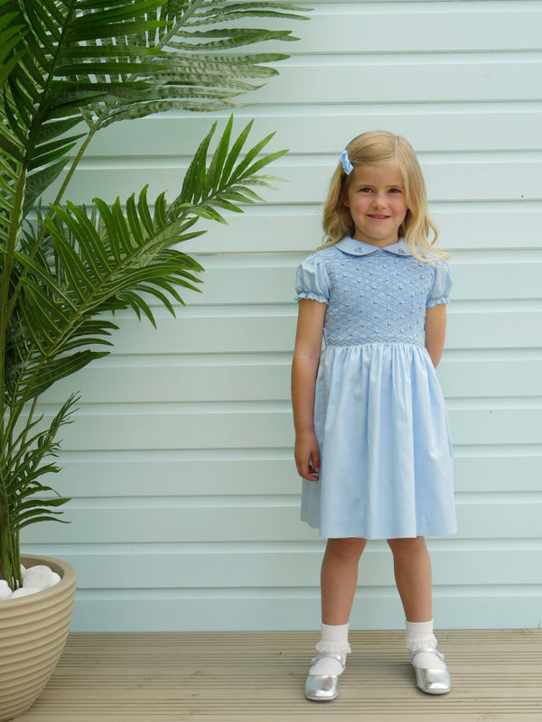 Girl in blue dress with smocked bodice, embroidered with roses, peter pan collar and gathered skirt.