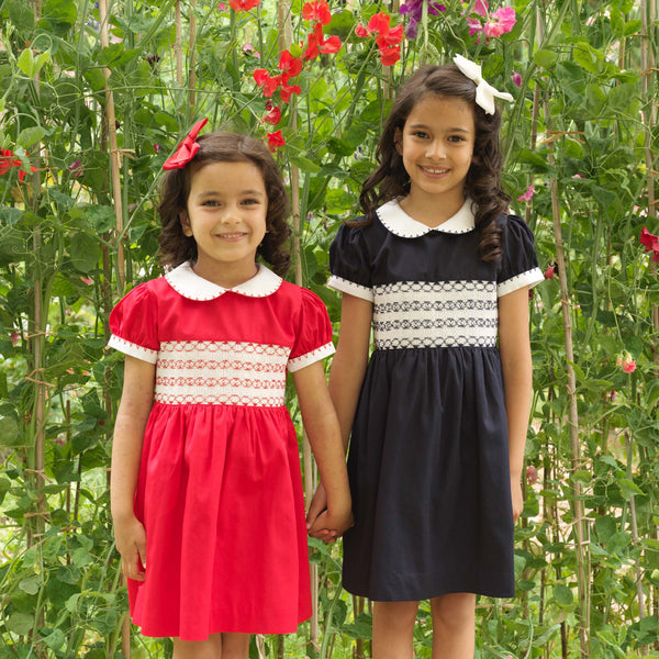Girls in matching navy and red smocked dresses and complementing hairbows.