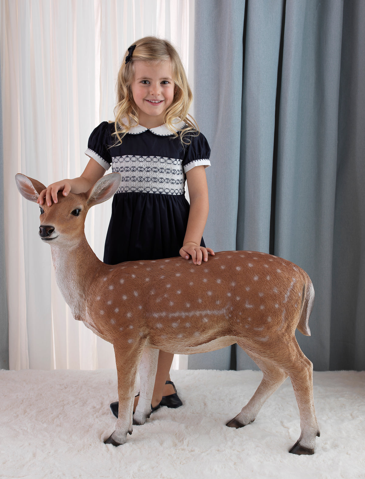 Girls wearing navy classic smocked dress, styles with matching hairbow and slippers.
