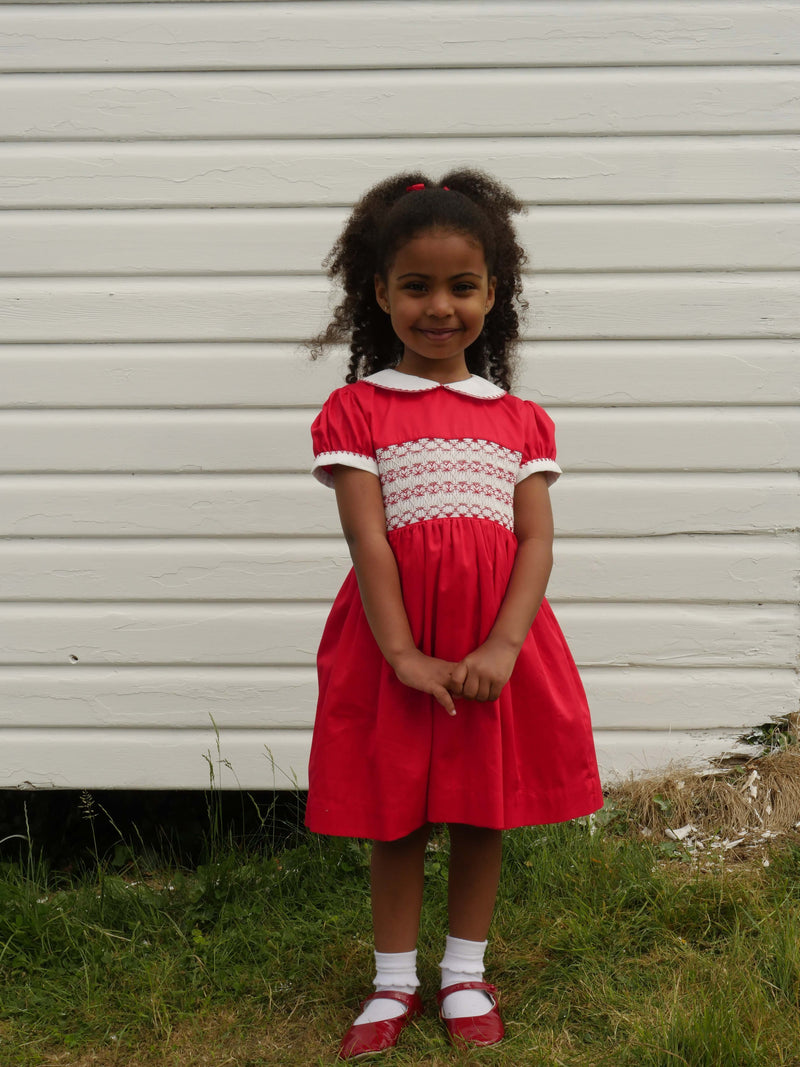 Girl wearing red classic smocked dress, styles with matching hairbow and slippers.