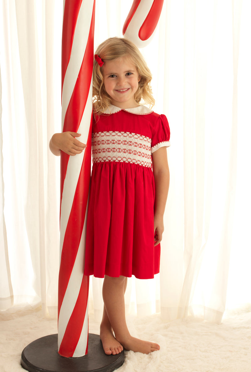 Girl wearing red classic smocked dress, styles with matching hairbow and slippers.