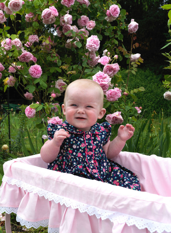 Baby in navy button-front dress with floral print, puff sleeves and pink ricrac trims and buttons.