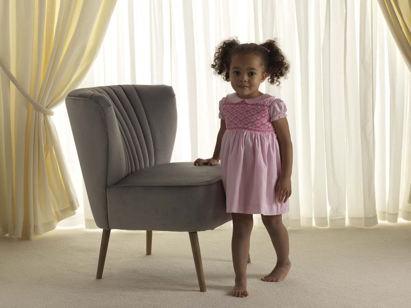 Baby girl in pink dress with smocked bodice, embroidered bows, peter pan collar and gathered skirt.