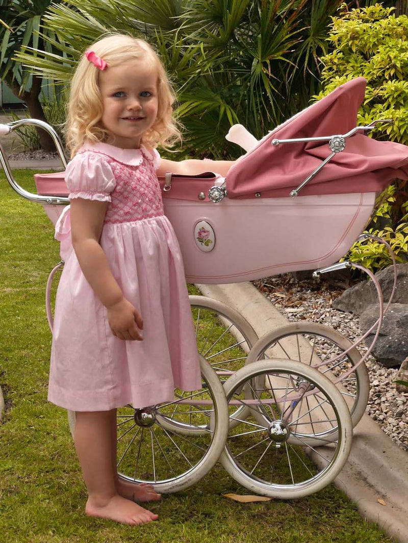 Baby girl in pink dress with smocked bodice, embroidered bows, peter pan collar and gathered skirt.
